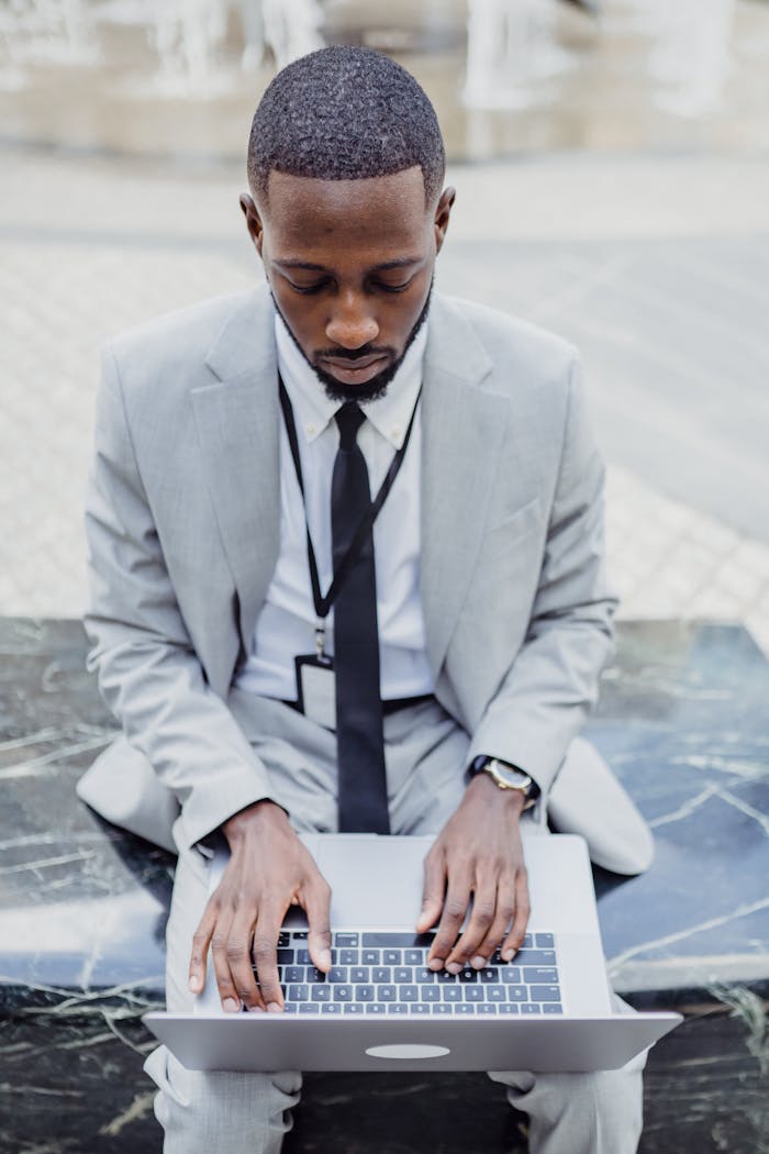 African American man in a suit using a laptop outdoors, focused on technology.