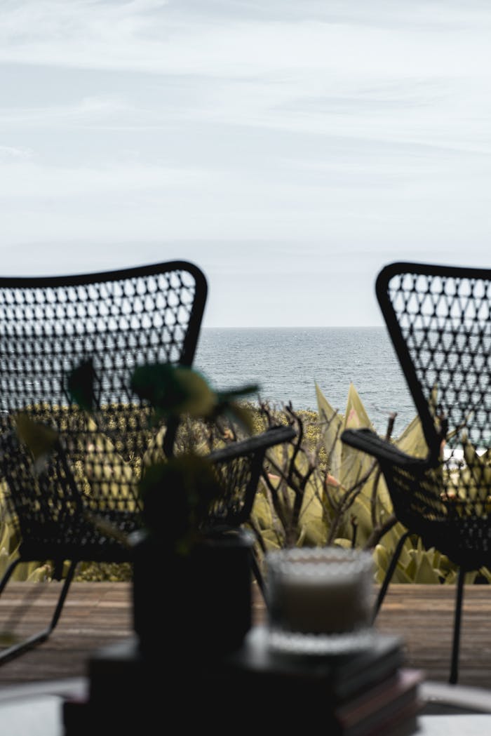 Wooden terrace with wicker armchairs placed nearby lush greenery in front of endless rippling seawater